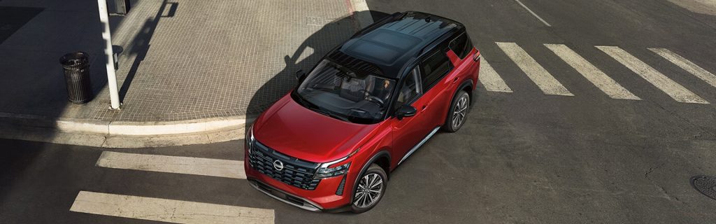 Red Nissan Pathfinder SUV crossing a city intersection from an overhead perspective.