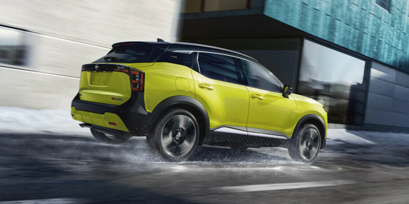 Lime green Nissan Kicks SUV driving through a wet urban street beside a modern building.